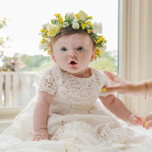 a baby girl in a christening gown wearing a flower crown