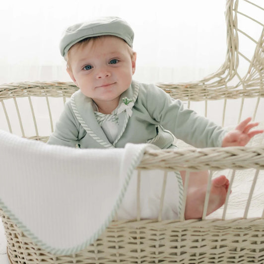 A baby boy in a basket wearing the Theodore baby boy suit.