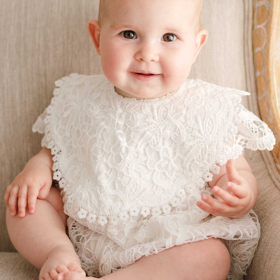 Baby girl wearing the Lola Lace Bib. The bib is designed with rich rayon blend with lace overlay in light ivory, cotton lace accents the edge and secures with a button.