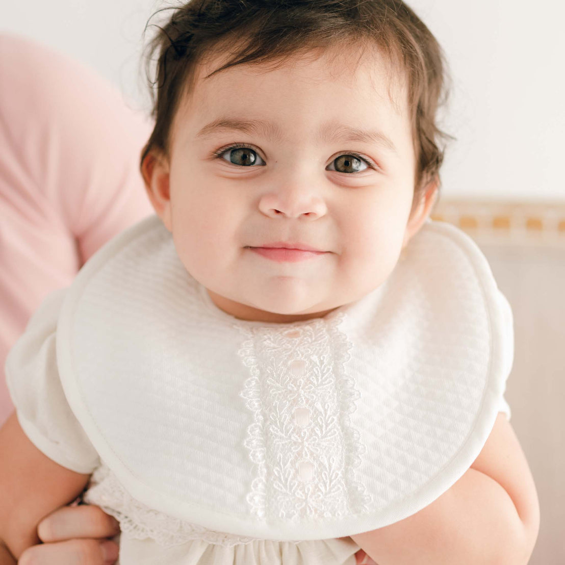 Close-up of a smiling newborn wearing an Emma Bib, looking at the camera with wide eyes.