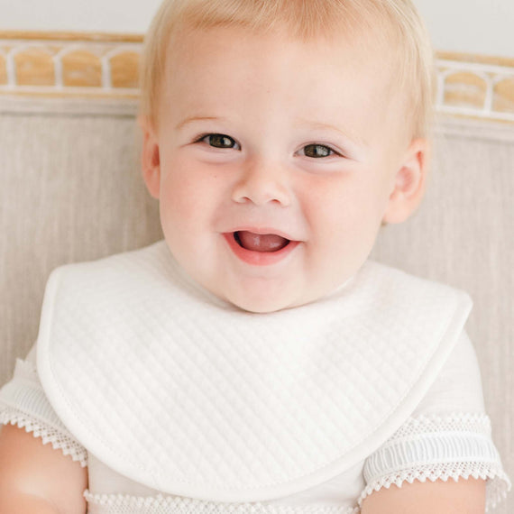 Baby boy smiling wearing a white christening bib.