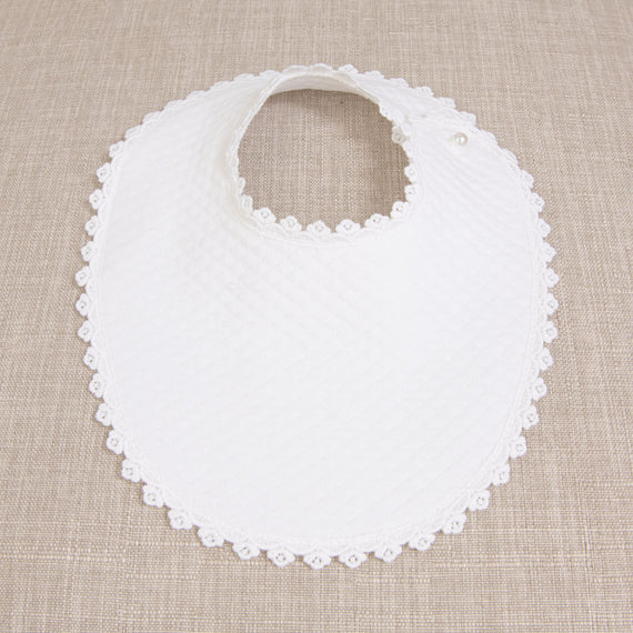 Melissa Bib with a textured design and scalloped lace edges, placed on a beige fabric background.