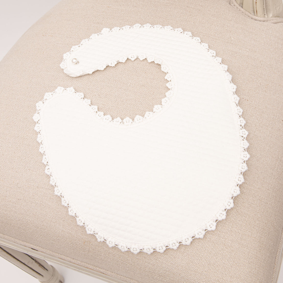 An upscale, Rose Accessory  bib with lace trim is on a beige fabric surface, close-up view.