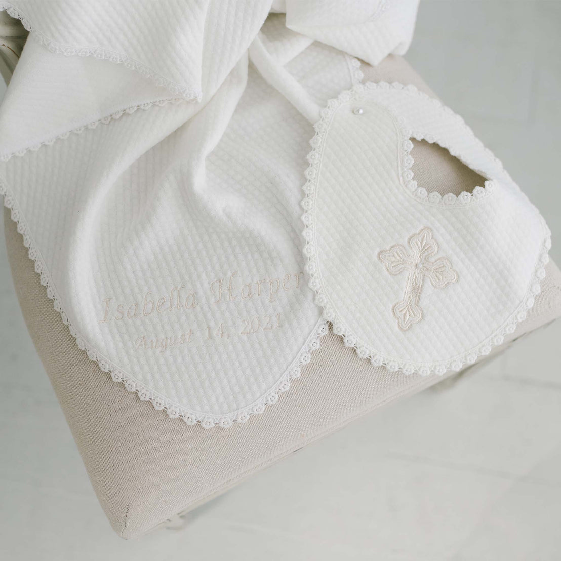 A personalized Baby Girl Blessing Gift Set by Baby Beau & Belle featuring a white bib and towel set with embroidered details and lace trim, showcasing the name "Isabella Harper" and the date "August 14, 2023".