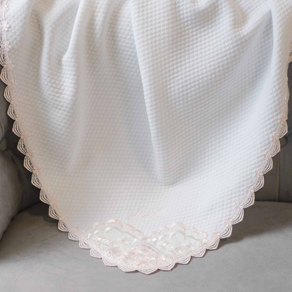 White Joli Personalized Blanket with intricate lace detailing and the word "faith" embroidered near the hem, displayed on a soft gray background.