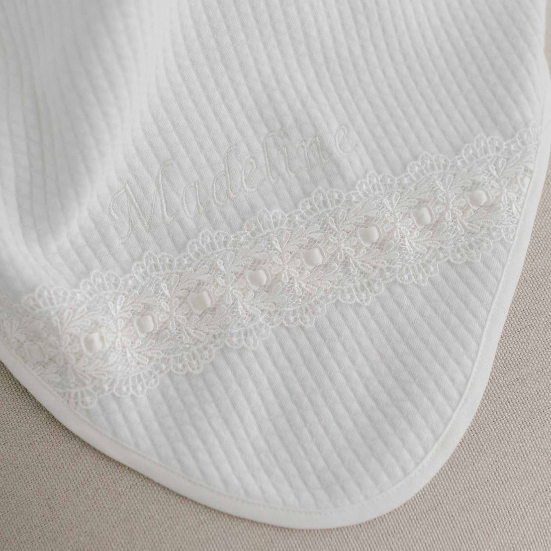 White fabric baby bib with delicate lace detail and pearls, featuring the embroidered name "Madeline" in an elegant script font. 
