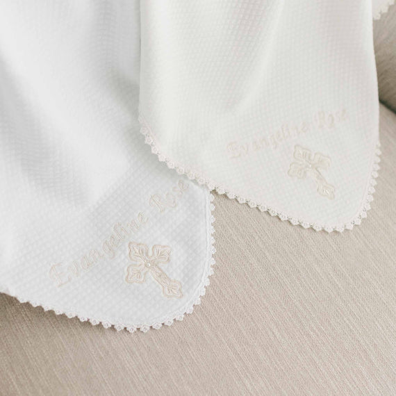Two white personalized cross blankets embroidered with the name "Evangeline Rose" and a cross design, featuring intricate scalloped edges and an upscale heirloom quality.