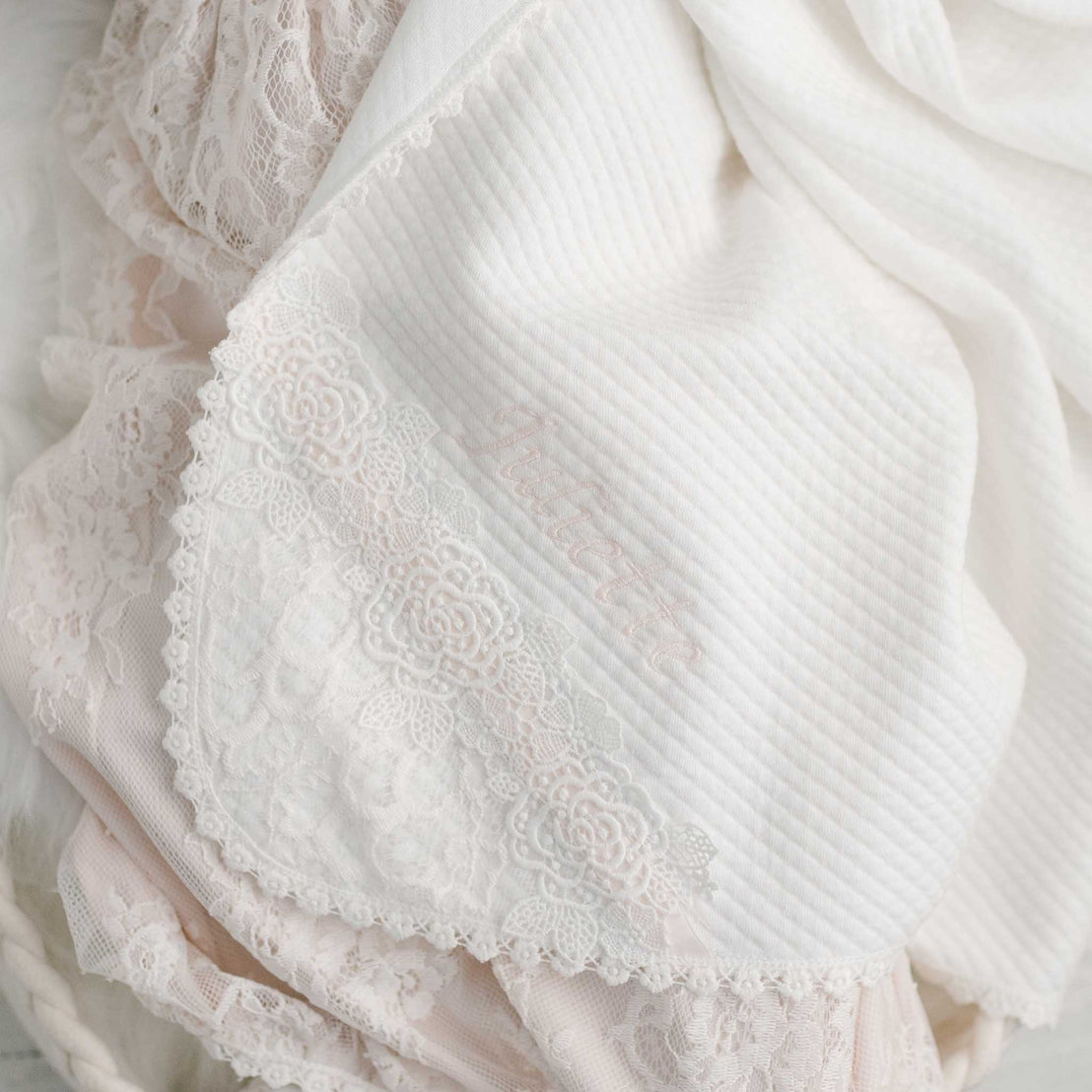 Close-up of the Juliette Blanket, an upscale, handcrafted white fabric with embroidered details and vintage lace, featuring a visible texture of soft, intricate patterns.