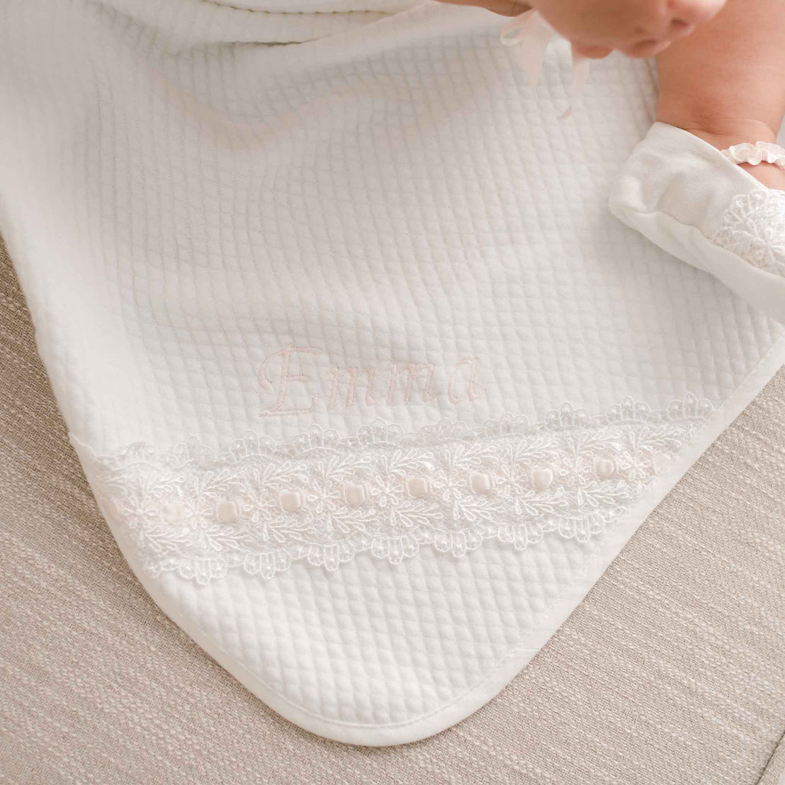 A close-up image of a baby wrapped in an Emma Personalized Blanket, featuring delicate lace detailing along the edge, perfect for a christening.