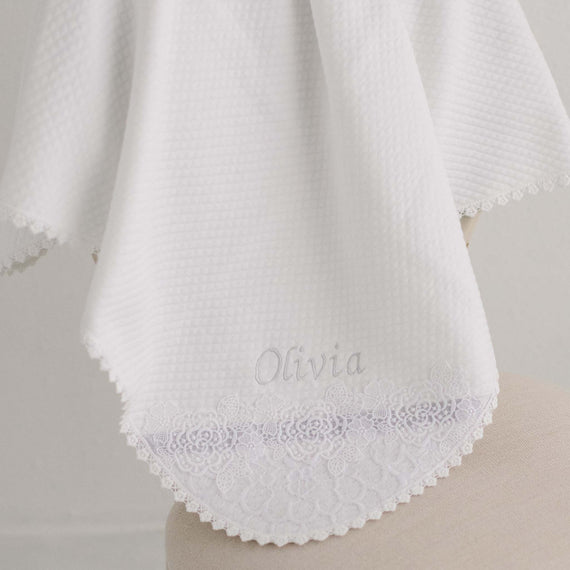 Boutique Olivia Personalized Blanket draped over a stand, featuring intricate lace detailing along the border and the name "Olivia" embroidered in the center.