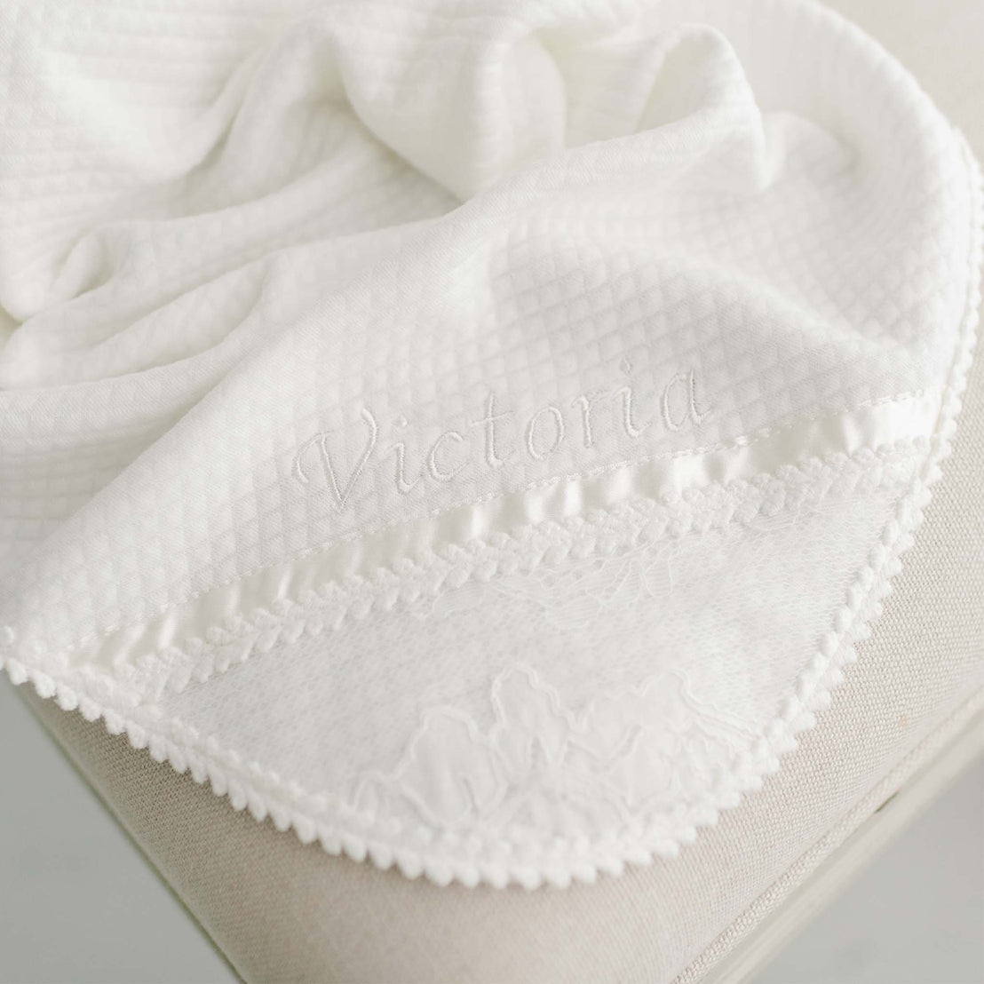 Closeup photograph of the corner of the quilted cotton Victoria baptism blanket. Personalized with the name Victoria embroidered in the corner.