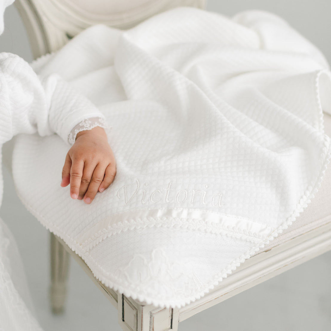 Alternative photo of the Victoria personalized baptism blanket on chair. Baby girls hand resting on corner. 