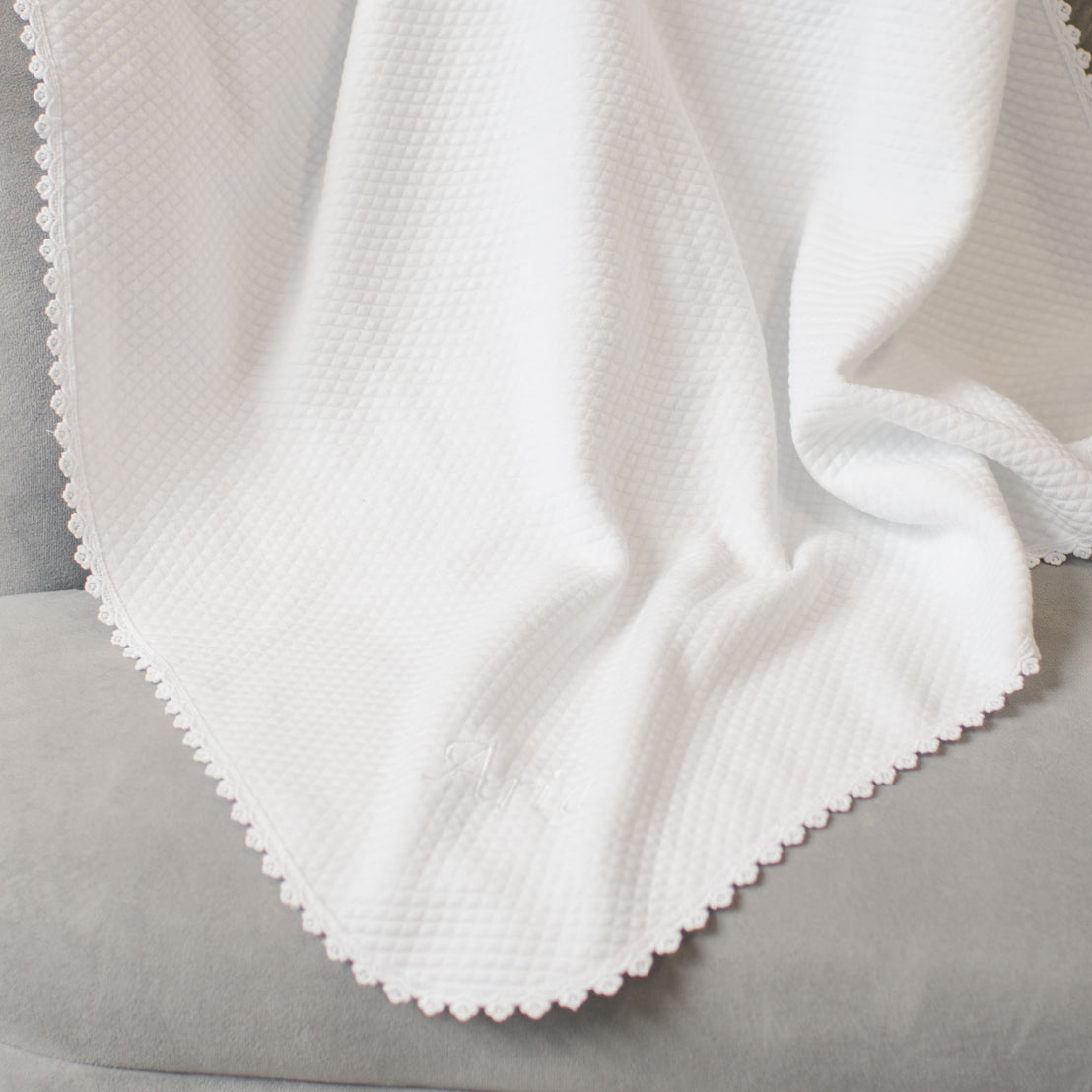 Close-up of a white textured cotton Aria Personalized Blanket with delicate embroidery detail, draped over a grey cushioned surface.