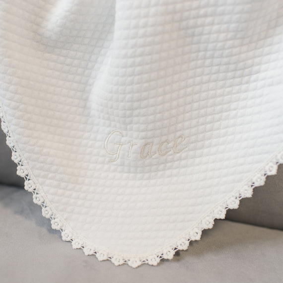 A close-up of a white Grace Personalized Blanket with waffle texture and delicate Grace lace edging, embroidered with the word "grace" in cursive script.