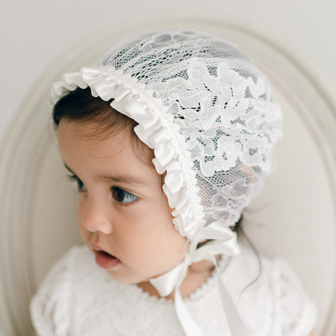 Baby girl wearing a lace baptism bonnet - part of the Victoria Christening Collection.