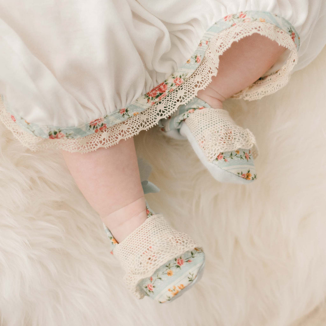 Detail of the "Powder Blue" variant of the Eloise Layette Gown skirt and Eloise Booties. The booties match the Eloise floral striped material with the natural color lace across both the skirt and toe.