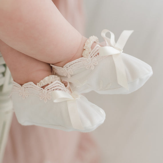 Close-up of a baby’s feet wearing Joli Booties with lace and ribbon details, held gently during a baptism.