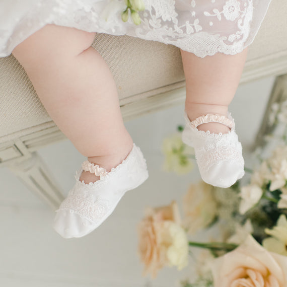 A close-up image of a baby's feet in Melissa Booties, delicately hanging over a chair with soft focus roses and flowers in the background.