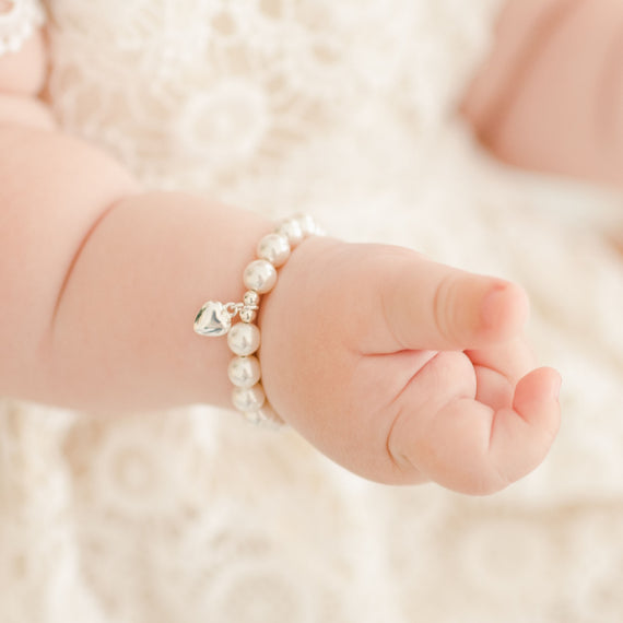 Baby girl wearing the white luster pearl bracelet around her wrist, part of our baby jewelry collection.