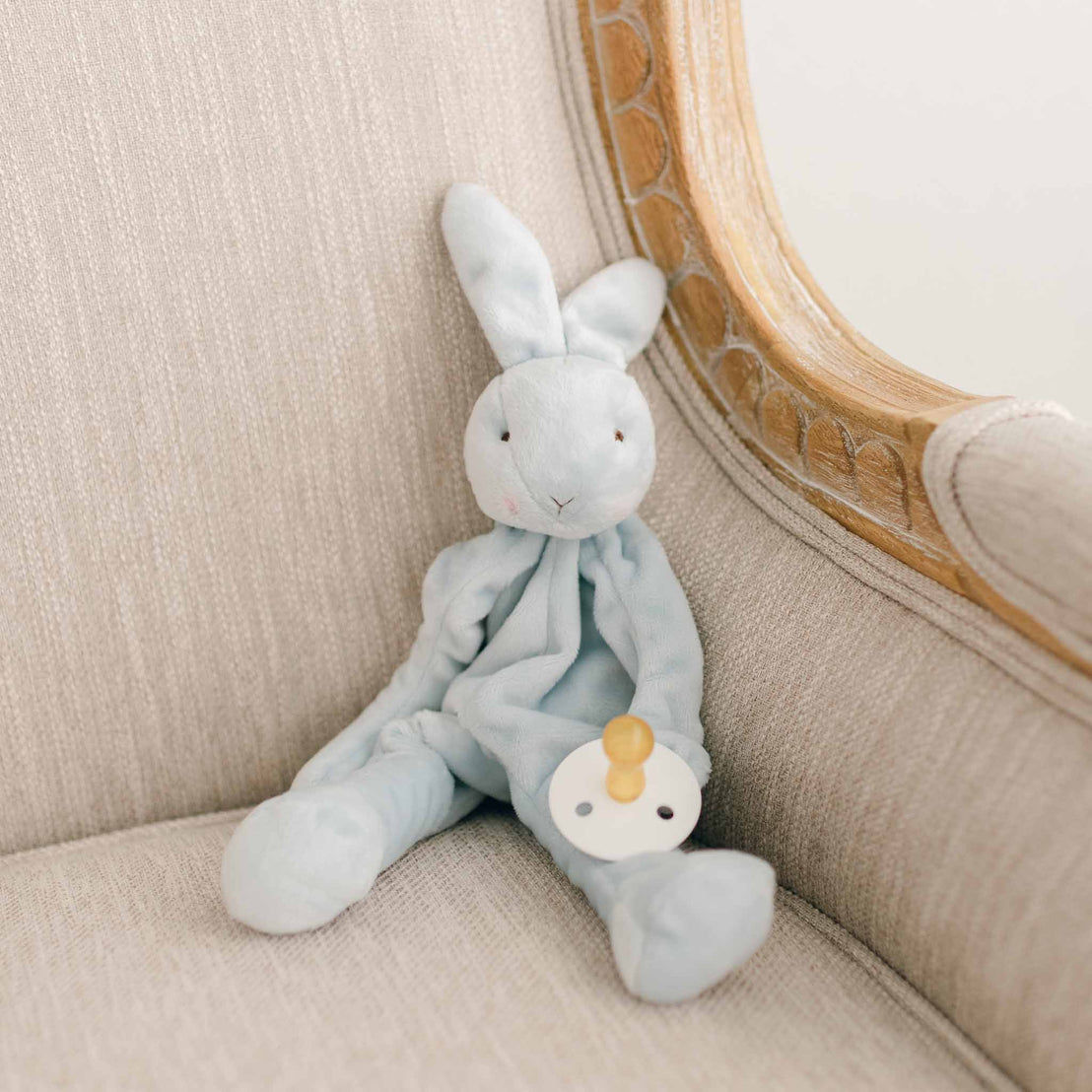 Photo of a blue bunny stuffed animal sitting on a chair. The bunny is able to function as a pacifier holder