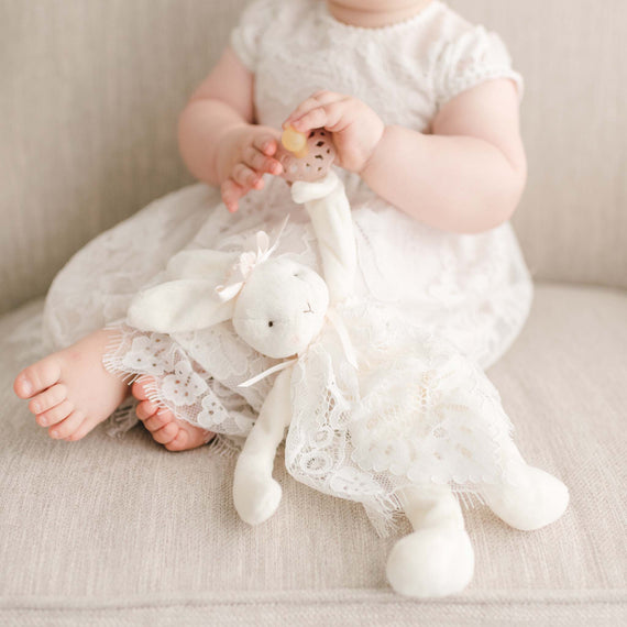A bunny buddy toy wearing lace from the Victoria gown, holding a baby pacifier. 