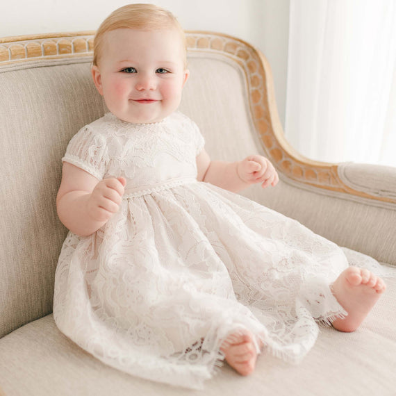 Baby girl sitting and wearing the pink Victoria Puff Sleeve Christening Dress. The dress made with an embroidered ivory lace and lined with pink silk Dupioni.