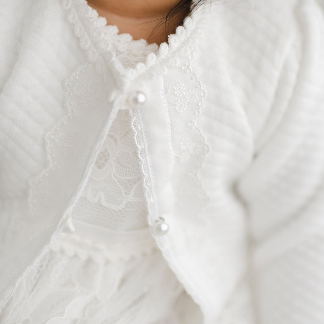 Close-up details of button and embroidery on the middle of the Victoria quilted cotton sweater. 