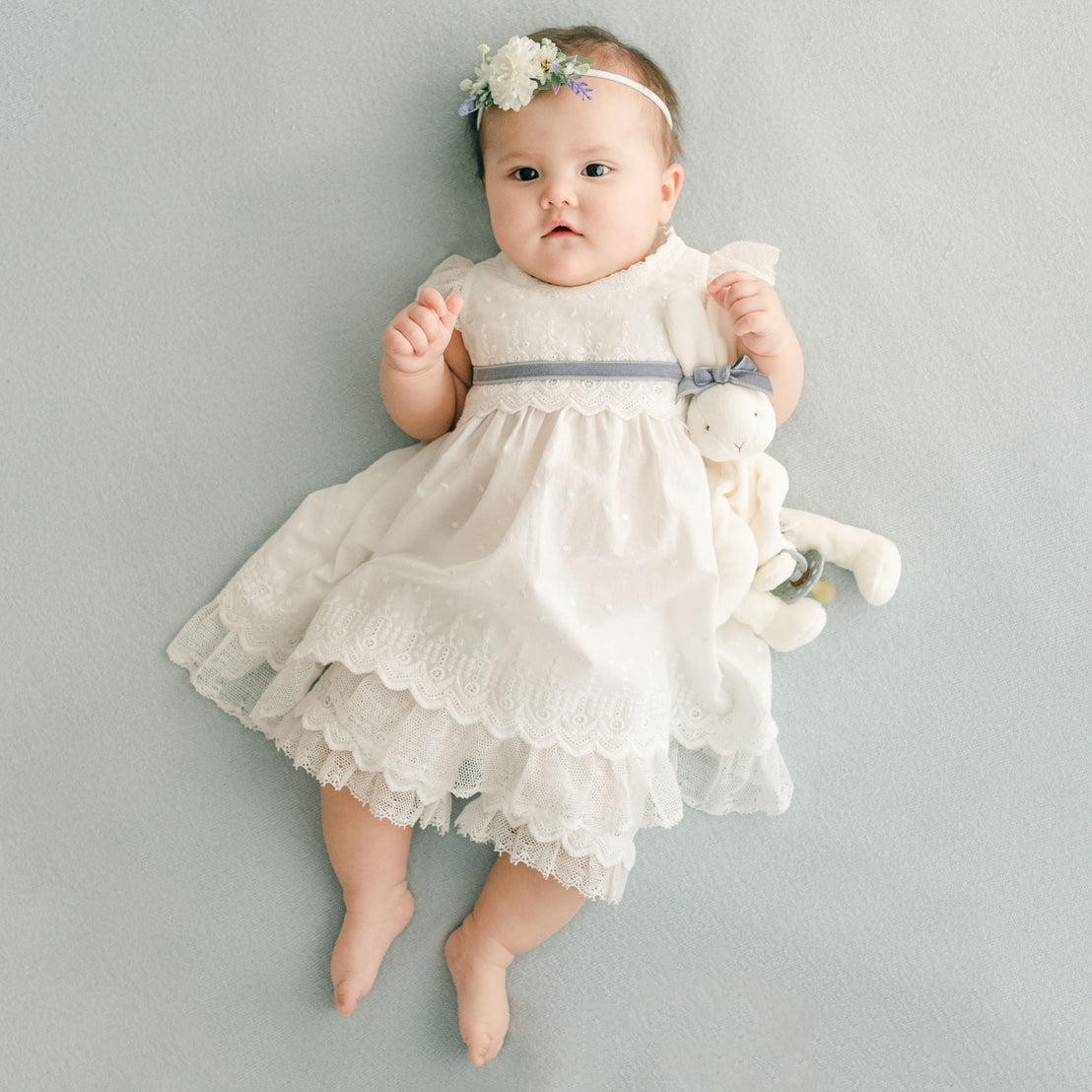 Baby girl wearing the Emily Dress and Bloomers with heather sash. She is also wearing the Emily Flower Headband.