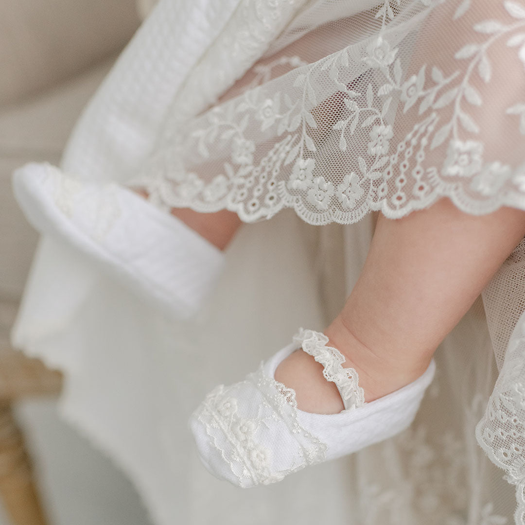 Close-up of a baby's feet adorned with Eliza Booties, gently held by an adult's hands dressed in a white, lacy garment.