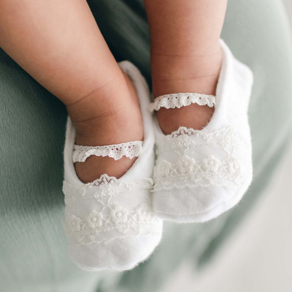Close-up of a baby's feet wearing the Ella Booties. Crafted with a soft textured cotton in white with a light ivory floral lace and ivory elastic lace strap.