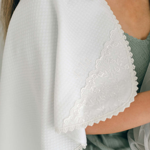 A close-up of a person's shoulder draped in the Ella Personalized Blanket with intricate floral lace trim and personalized embroidery spelling "Ella."