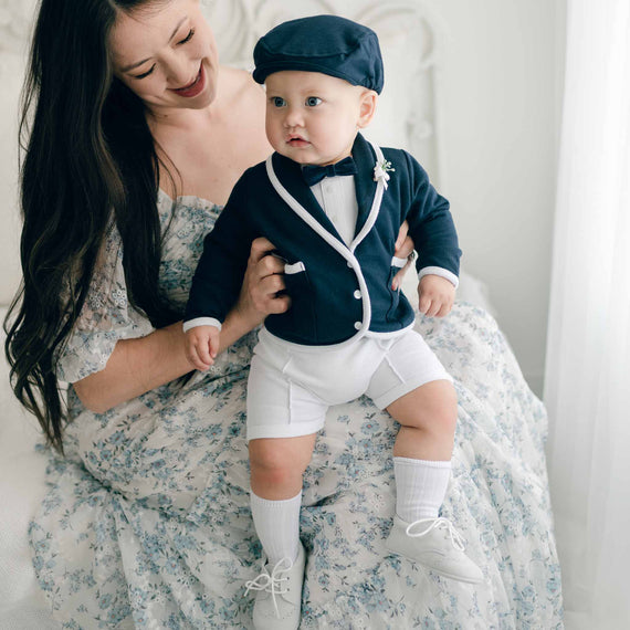 Baby boy with his mother. He is wearing the Elliott 3-Piece Shorts Suit, including the jacket, shorts, and onesie (and matching Navy Elliott Newsboy Cap). He is also wearing the Elliott Bowtie and Boutonniere.