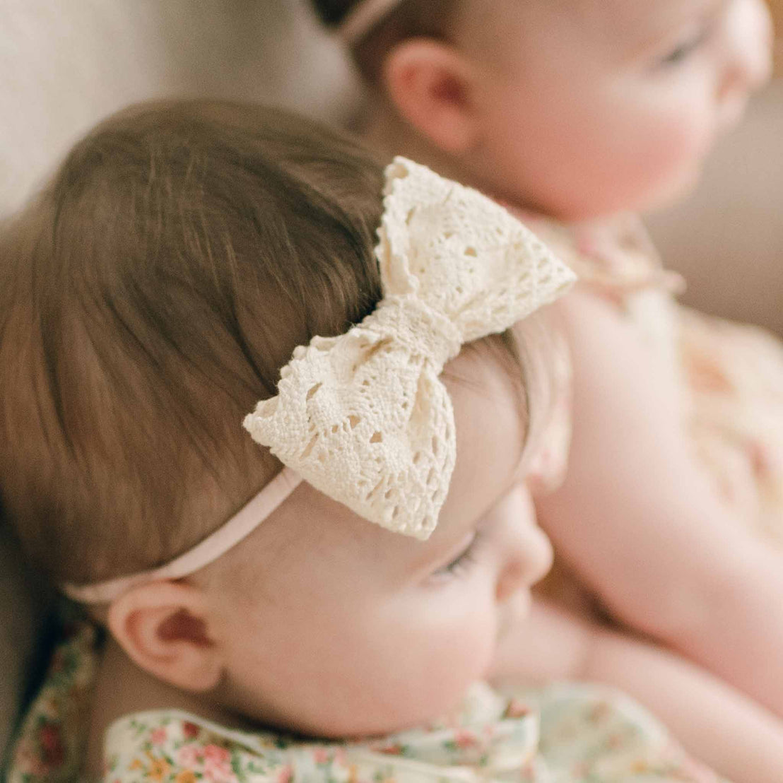 Close up detail of a newborn baby girl wearing the Eloise Bow Headband made with the matching lace used on the bodice on her Eloise Romper Dress on a hand-stretched nylon band,
