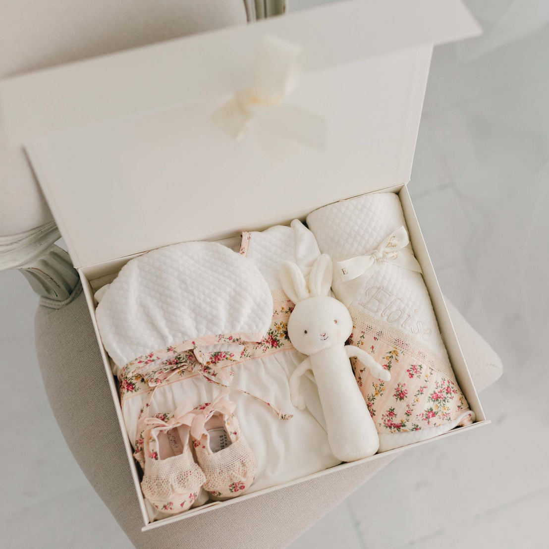 The "Blush" Eloise Newborn Gift Set in the gift box, including the Layette Gown Bonnet, Booties, Bunny Chime, and Blanket.