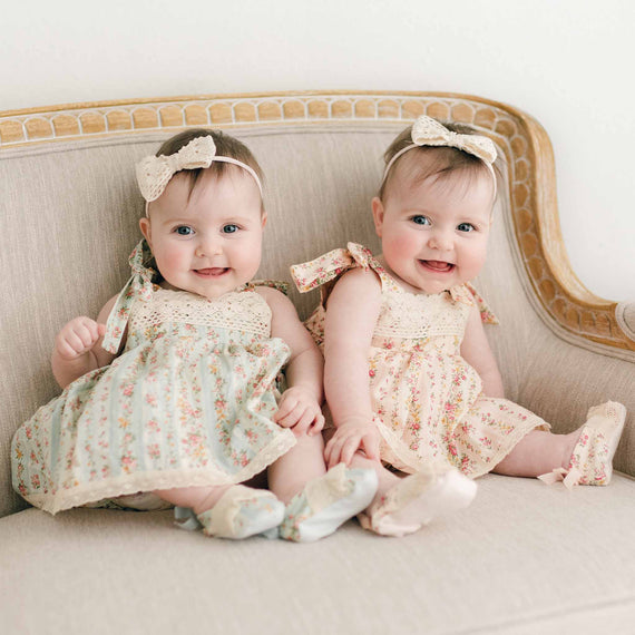 Two twin baby girls wearing the Eloise Romper Dress. One in Powder Blue and the other in Blush.