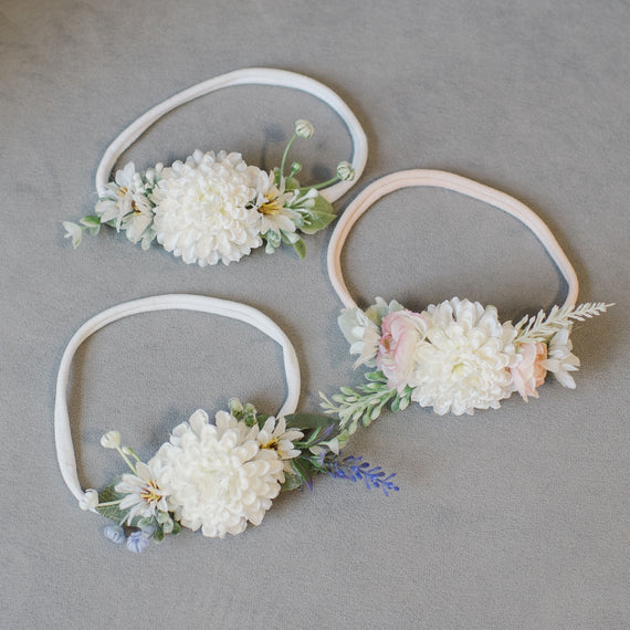 Flat lay showcasing the Emily Flower Headbands, featuring color variations in white, mauve, and heather. Hand crafted on a gentle hand-stretched nylon band, embellished with delicate flowers and verdant greenery.