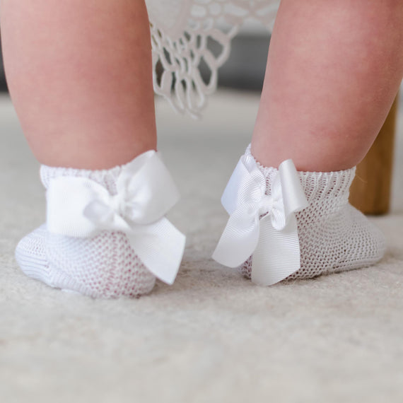 Close-up of a baby's feet wearing Garter Stitch Socks with Bow, standing on a soft beige surface.