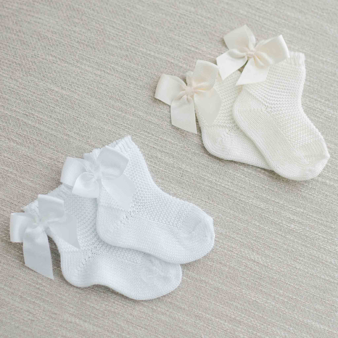 Two pairs of Garter Stitch Socks with Bow, presented on a soft beige fabric background.