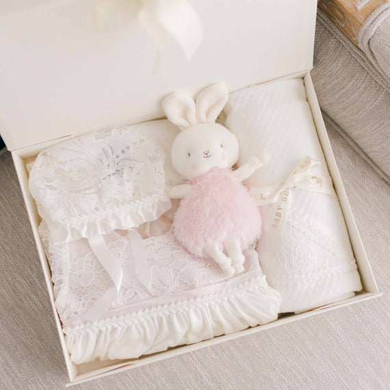 A baby gift set, part of the Victoria Christening Collection. Shown are baby bonnet, plush doll, layette gown and personalized blanket. 