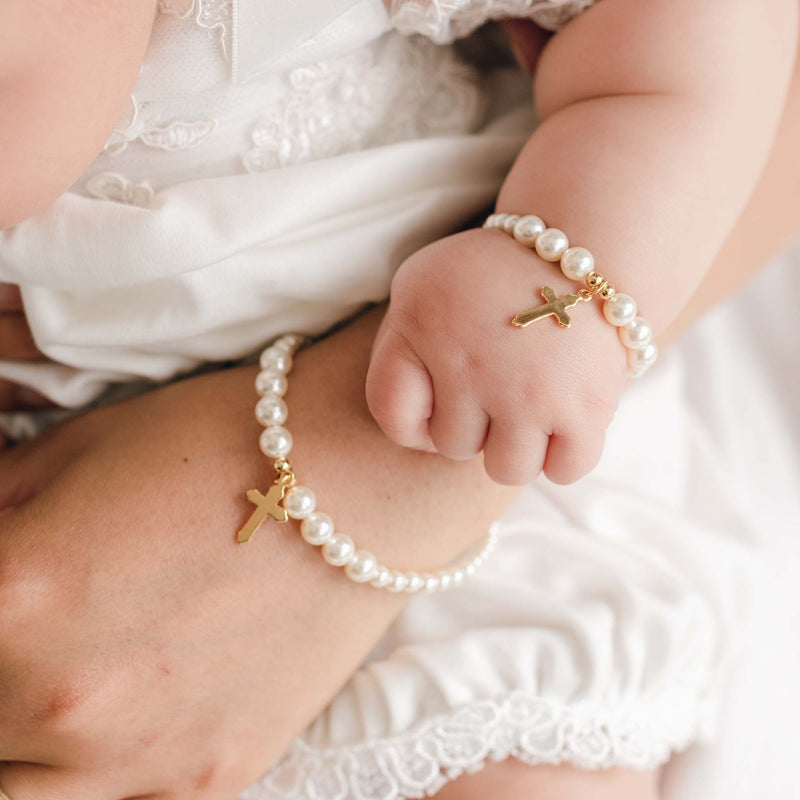 Close-up of a hand and child's hand holding together, both wearing pearl bracelets with gold crosses.