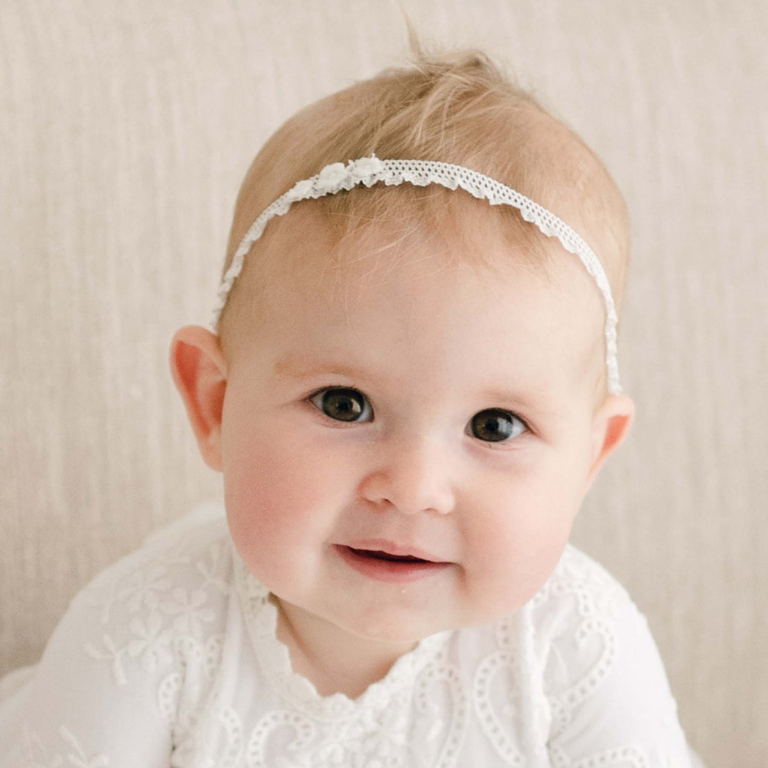 Baby girl sitting on a couch wearing an Eliza lace headband. 