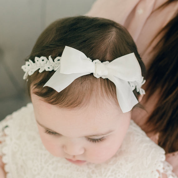 Close-up of a baby wearing a Grace Headband with a silk ribbon bow. The focus is on the baby’s head looking downward.