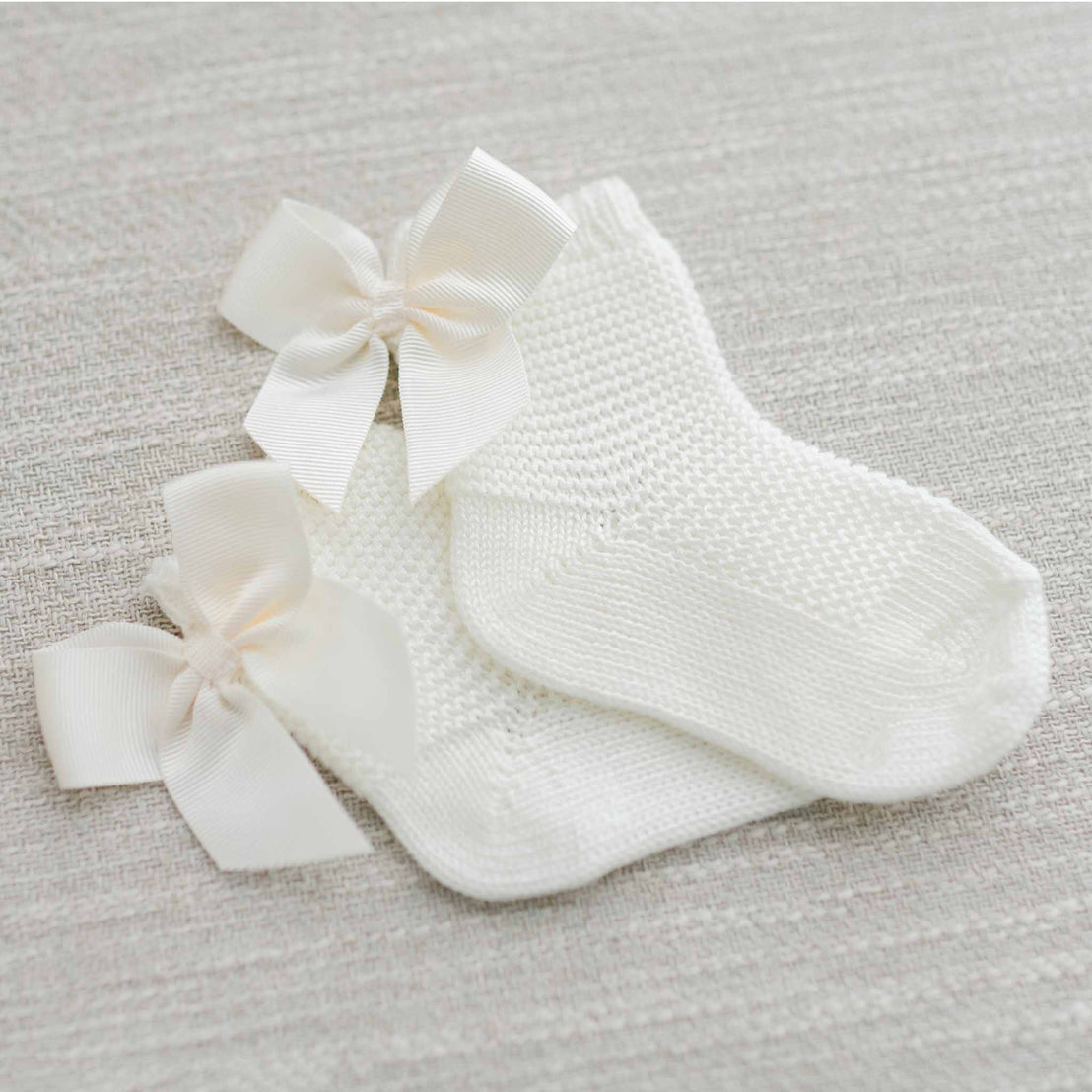 A pair of Garter Stitch Socks with Bow adorned with delicate white satin bows, presented on a soft-textured light gray background.