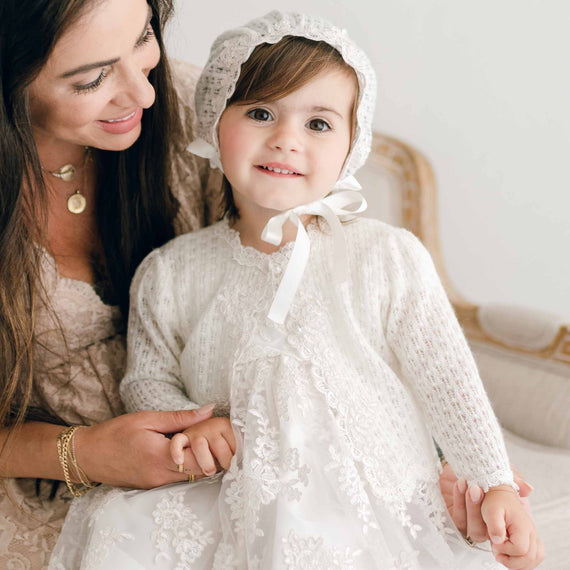 Baby girl with mom wearing Penelope knit baptism sweater and bonnet. 