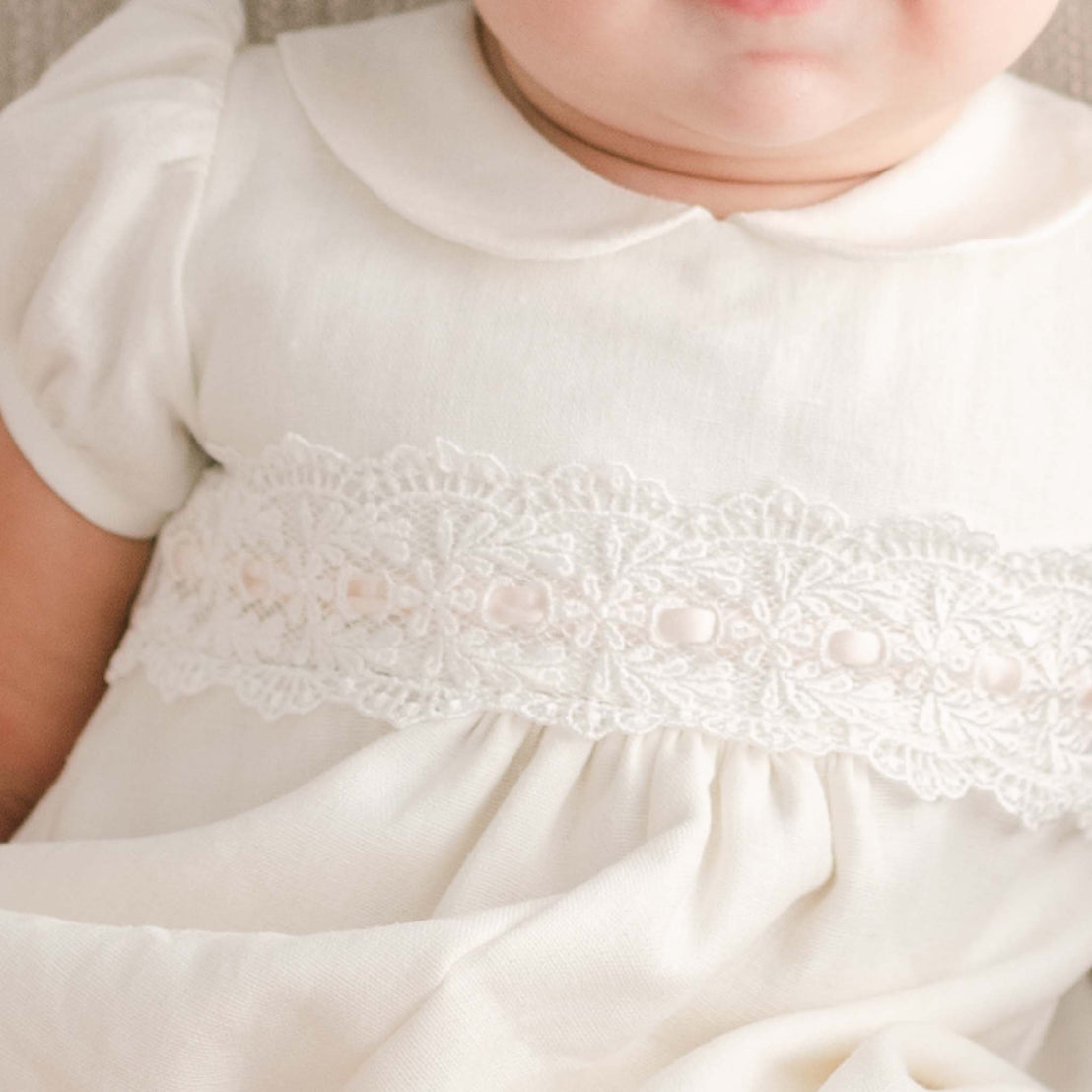 Close-up of a baby wearing an Emma Convertible Skirt & Romper Set with detailed lace embroidery for a baptism. The focus is on the lace and the soft texture of the fabric.