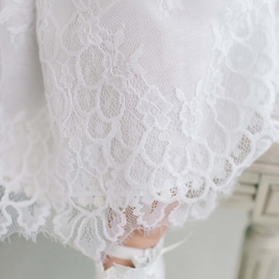 Close-up view of a bride's Olivia Christening Gown with delicate floral patterns, highlighting intricate craftsmanship and heirloom elegance.