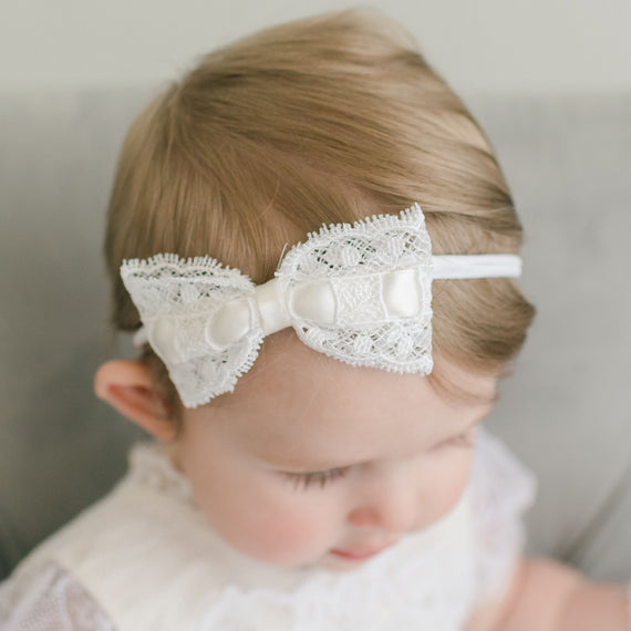 Close-up of a baby with a delicate white lace headband, specifically an Aria Lace Bow Headband, showcasing the white edge lace with white silk ribbon bow.