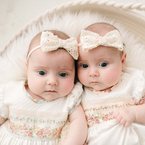 Two twin newborn baby girls wearing the Eloise Bow Headband. A natural lace bow made with the matching lace used on the bodice of the Eloise Romper Dress on a hand-stretched nylon band.