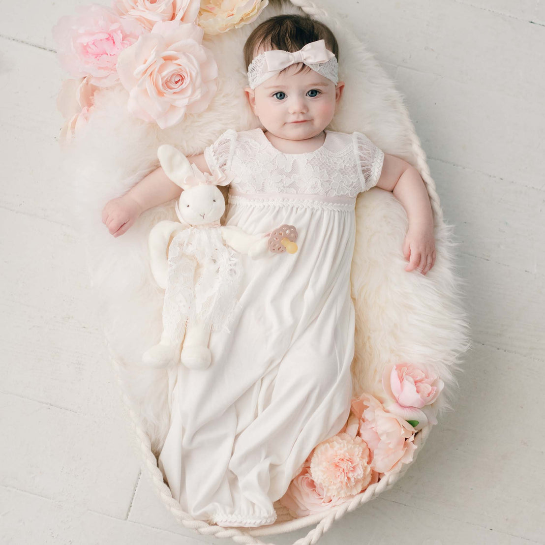 Flat lay photo of baby girl smiling wearing a cotton layette gown and the Victoria lace christening headband with bow.