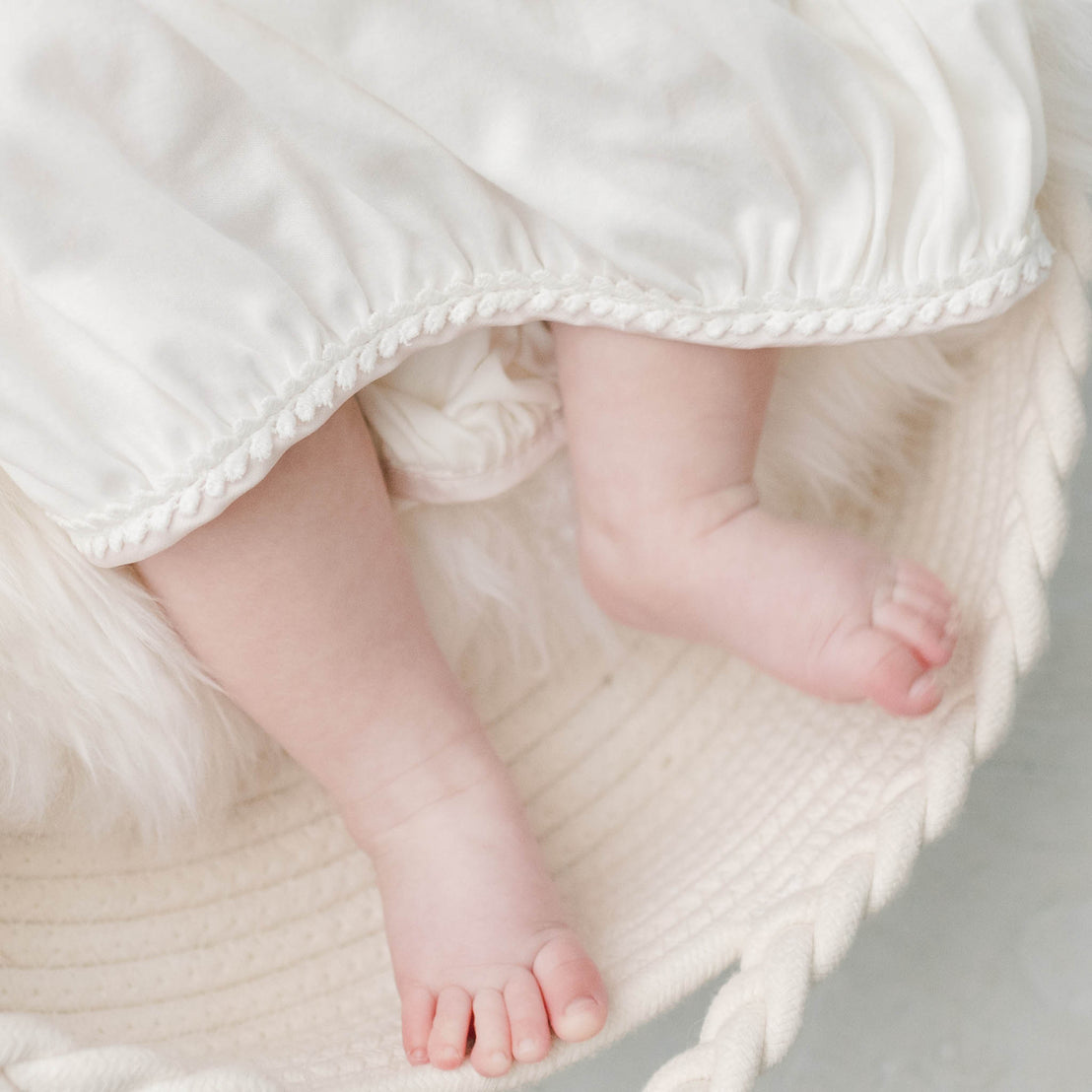 Baby girl toes sticking out of the Victoria Layette Gown, edge embroidered with a beautiful floral lace. 